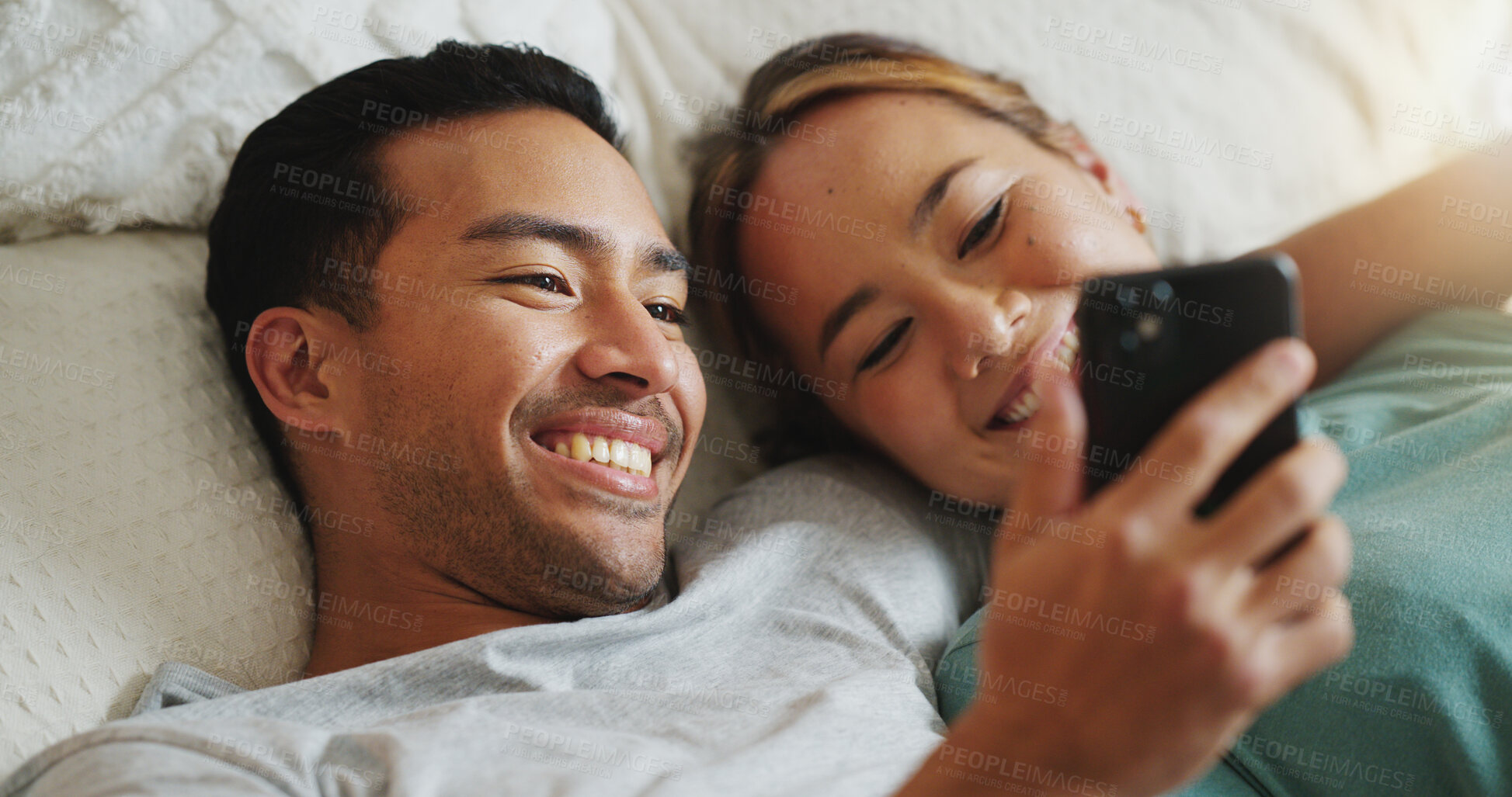 Buy stock photo Phone, social media and communication with a couple in bed to relax, laughing and relaxing in the bedroom of the home together. Diversity, internet and mobile with a man and woman happy in the house