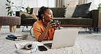Laptop, coffee and woman on the floor in living room of modern apartment reading information. Technology, relax and young African female student study and drink latte on computer in lounge at home.