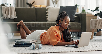 Laptop, typing and woman laying on the floor in the living room of modern apartment. Technology, elearning and young African female university student studying on a computer in the lounge at home.