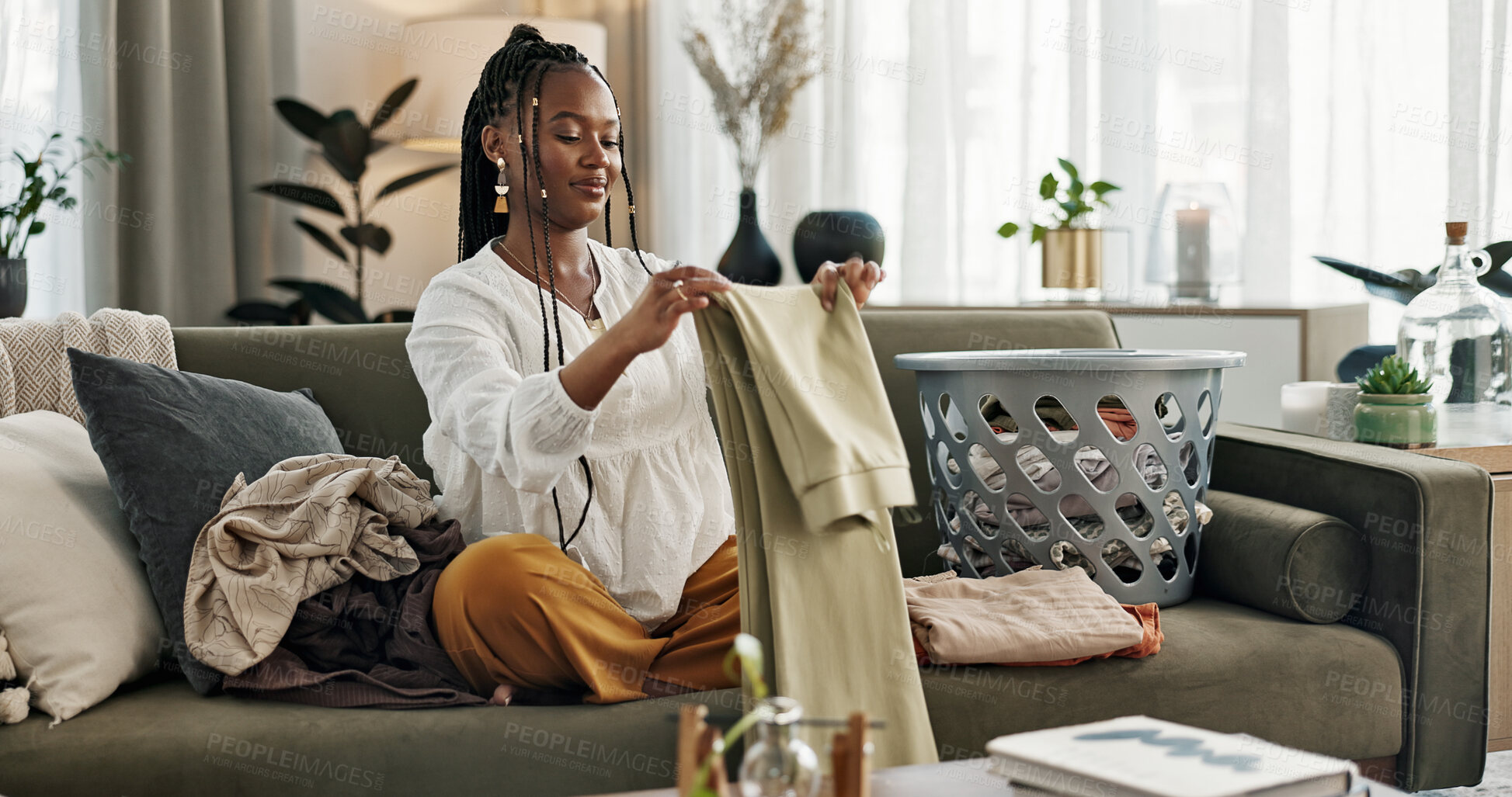 Buy stock photo Laundry, housework and a black woman folding washing on a sofa in the living room of her home to tidy. Smile, relax and a happy young housewife cleaning her apartment for housekeeping or hygiene