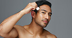 Face, pipette and Asian man with skincare, oil and dermatology on a grey studio background. Portrait, Japanese person and model with wellness, treatment and grooming product with aesthetic and glow