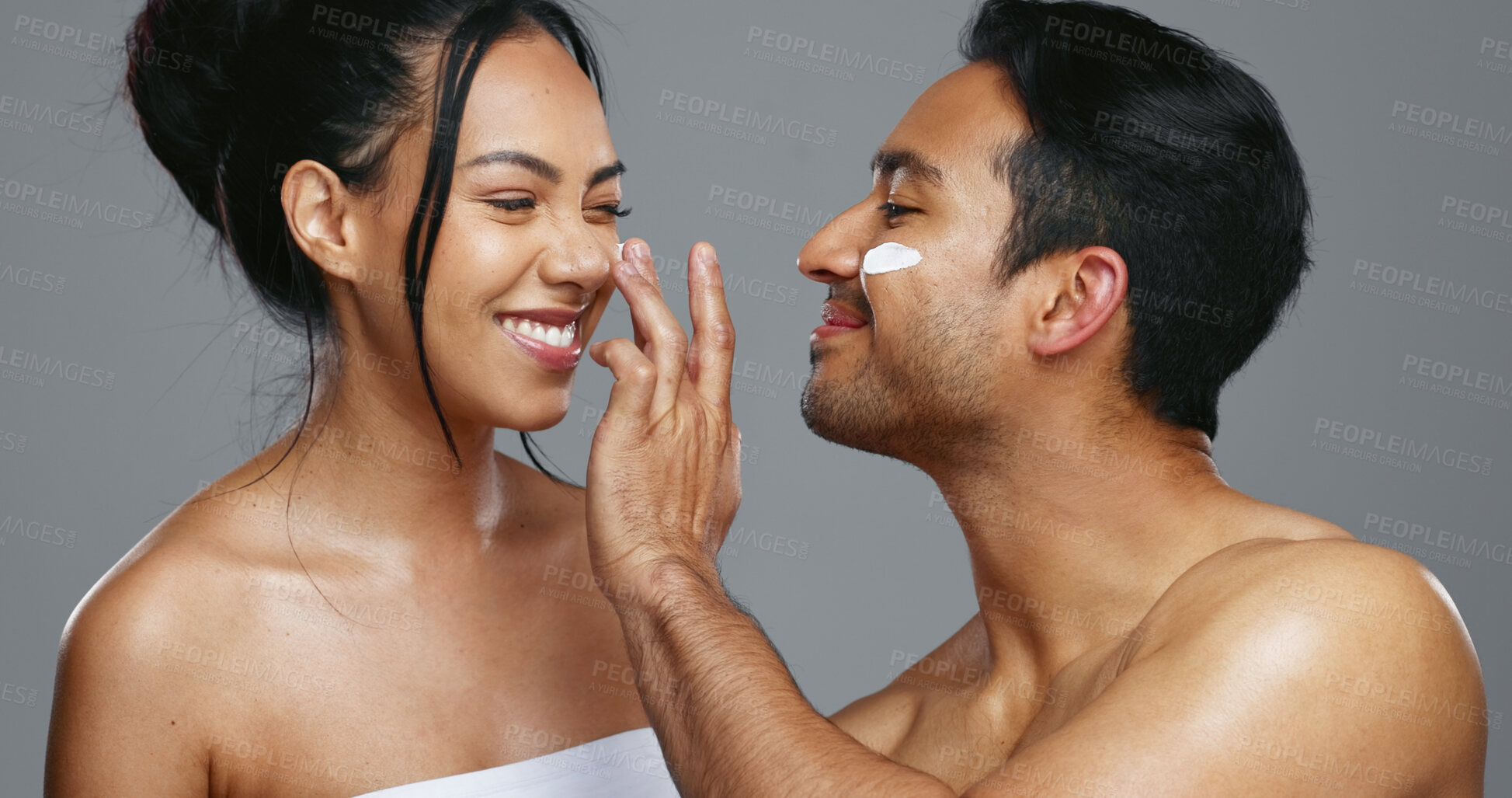 Buy stock photo Couple, smile and love for skincare, care and portrait with moisturizer in studio by gray background. Happy people, dermatology and hug for cosmetics, hydration and creme or love for skin treatment