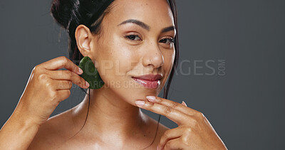 Woman, guasha and skincare for massage, facial and portrait or smile in studio by gray background. Happy model, cosmetics and dermatology in technique for beauty, self love and natural glow by tool