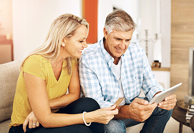 Buy stock photo Beautiful, smiling mature couple buying online, shopping on their digital tablet together on their home living room sofa. Husband making financial payments through internet banking with his wife