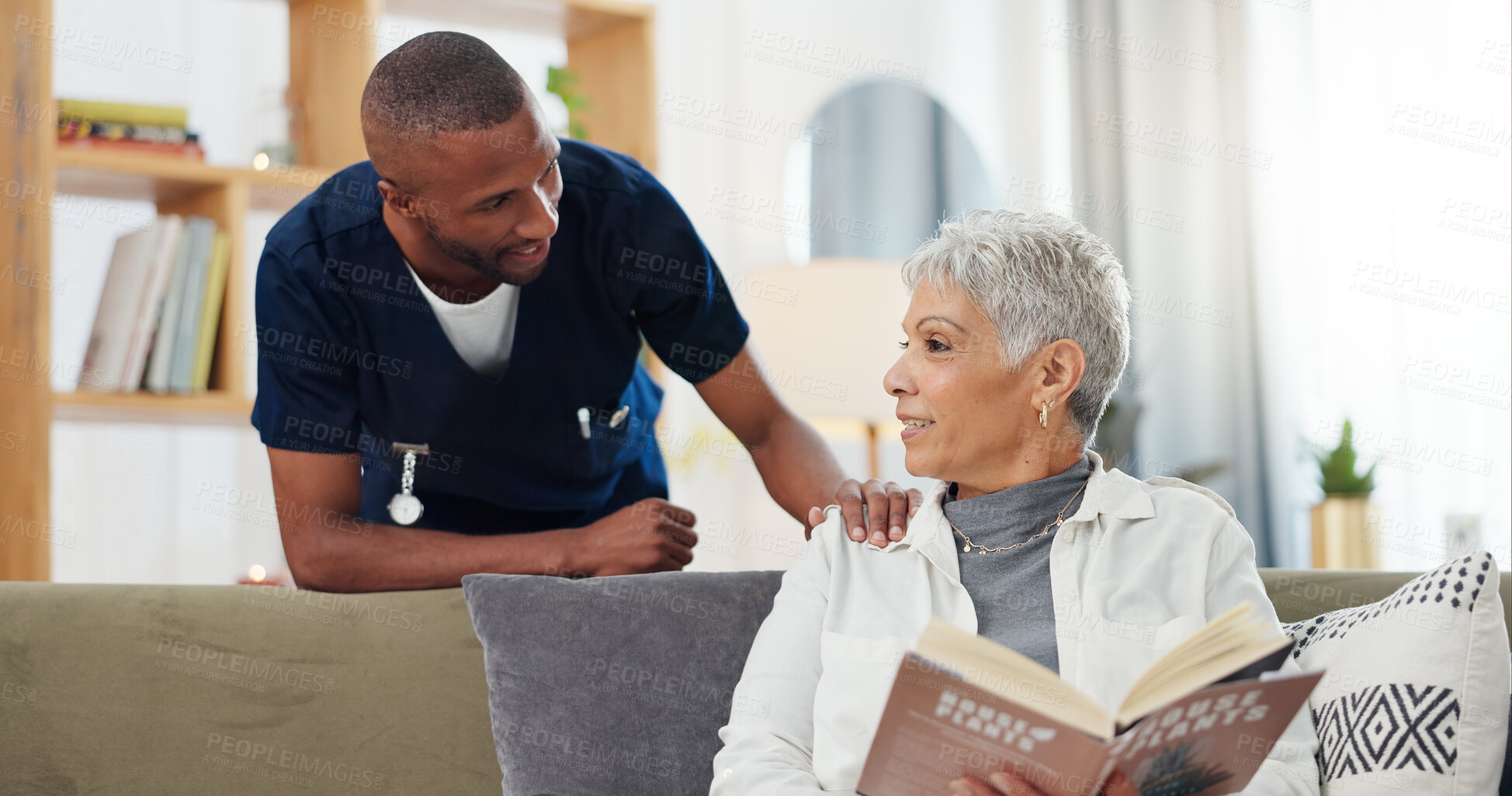 Buy stock photo Senior, woman and nurse on sofa with support, conversation and caregiver in living room of retirement home. Elderly, person and black man with kindness, happiness and discussion while reading a book