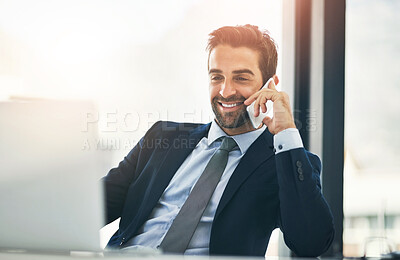Buy stock photo Shot of a handsome young businessman talking on a cellphone while working on a laptop in an office