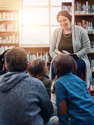 Buy stock photo Shot of a teacher reading to a group of elementary school kids in the library