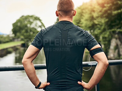 Buy stock photo Rearview shot of a sporty young man taking a break while exercising outdoors