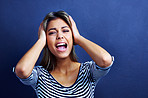 Woman, noise and cover ears in studio with stress, mental health and shouting with anxiety by blue background. Girl, person and model with tinnitus, frustrated and stop sound with hands on head