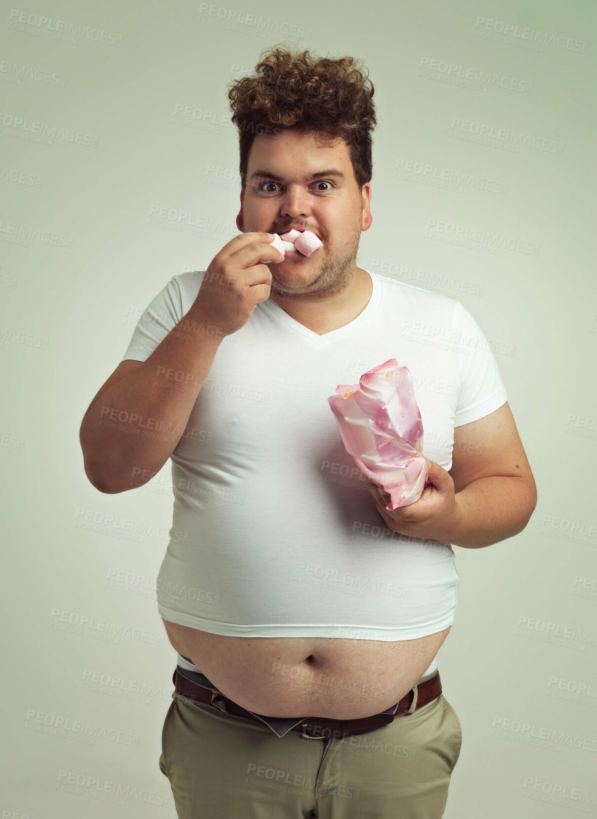 Buy stock photo Portrait, hunger and marshmallow with plus size man in studio on gray background for unhealthy eating. Food, hungry for sweets and candy with young person with snack bag or packet for greed or belly