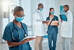Young african american female doctor working on a digital tablet and wearing a mask while working at a hospital with colleagues. Black female nurse doing research on a digital tablet at work at a clinic