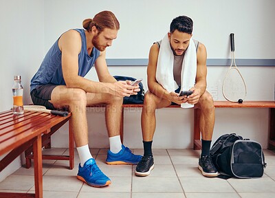 Buy stock photo Two players using their cellphones together. Young squash players reading text messages on their smartphones together. Friends relaxing in a gym locker room together before a match