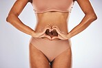 Woman in underwear, heart on stomach and healthy lifestyle for fitness, workout and diet on grey studio background. Female, lady and sign for love, healthcare and wellness with digestion or body care