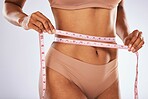 Measuring tape, stomach and woman in studio for wellness, weight loss and tummy tuck on grey background. Belly, measurement and girl model checking for progress, slimming and size after detox or diet