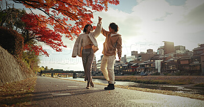 Buy stock photo Young couple, dancing or love in city by canal, autumn leaves or happiness in bonding in nature. Man, woman and care for together by red maple tree, romance and blue sky in tokyo town by urban houses