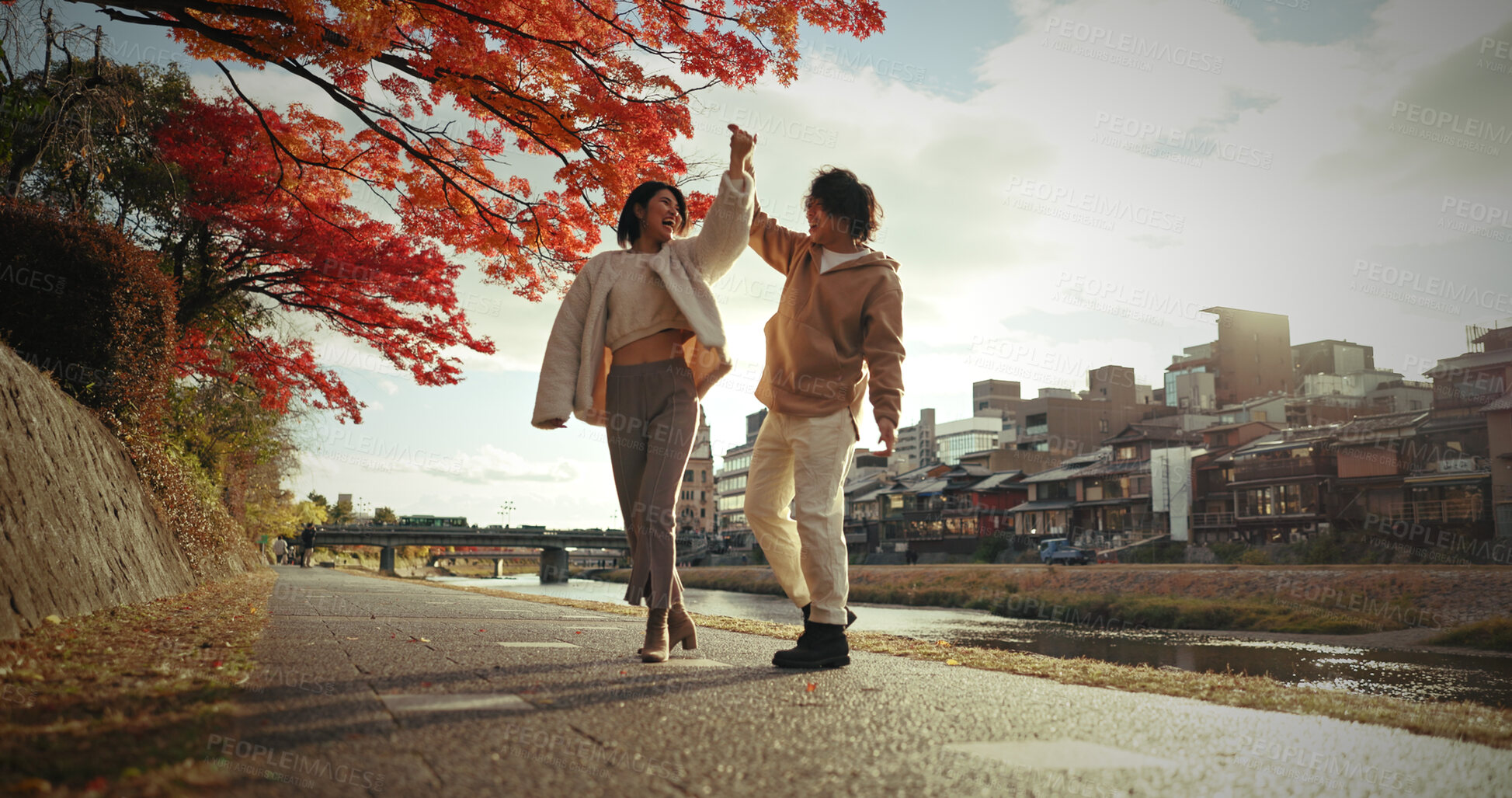 Buy stock photo Young couple, dancing or love in city by canal, autumn leaves or happiness in bonding in nature. Man, woman and care for together by red maple tree, romance and blue sky in tokyo town by urban houses