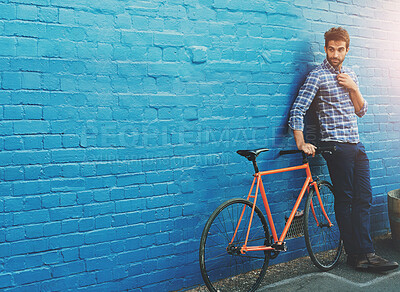 Buy stock photo Shot of a handsome young man posing with his bicycle against a blue wall