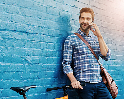 Buy stock photo Shot of a handsome young man leaning against a wall with his bike talking on a cellphone