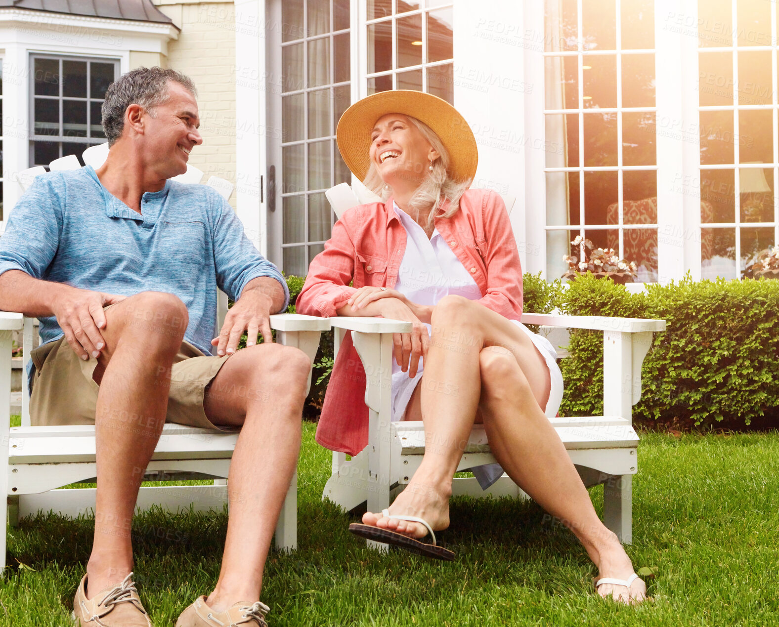 Buy stock photo Mature couple, lawn and relax on chair with funny conversation, bonding and care in summer at house. Man, woman and happy with laughing at comic memory, talking or chat on grass in backyard garden