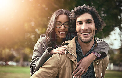 Buy stock photo Portrait of a cheerful young couple having a piggyback ride while looking at the camera outside in a park
