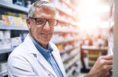 Buy stock photo Portrait of a cheerful mature male pharmacist getting medication from a shelf while looking at the camera in a pharmacy