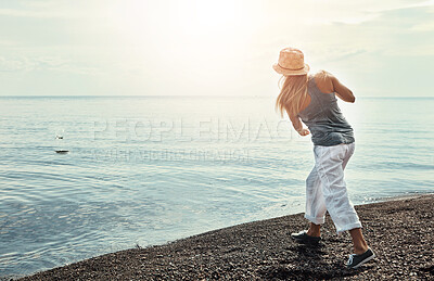 Buy stock photo Beach, coast and woman skipping rocks outdoor in summer for hobby, leisure or vacation from back. Earth, ocean and sky with person throwing stone into sea or water for break, holiday or weekend trip