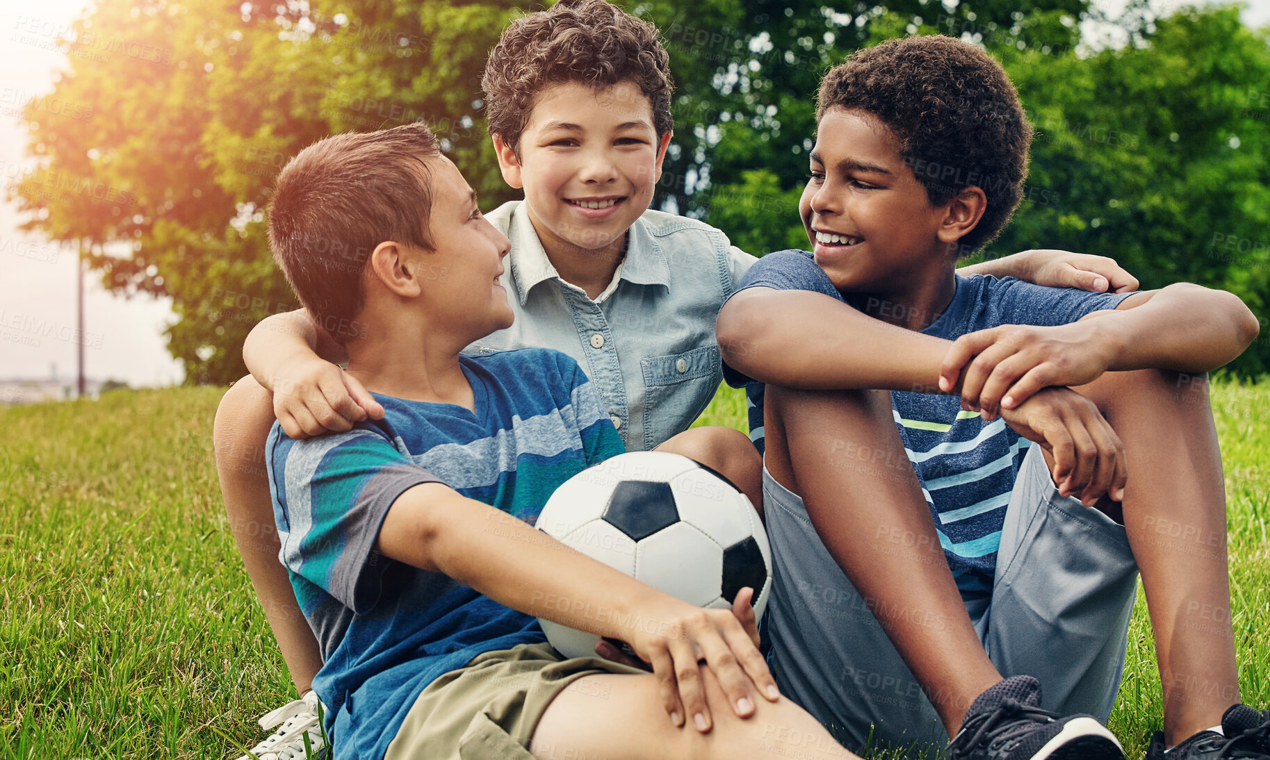 Buy stock photo Children, boys and sitting on grass with soccer ball in park for happiness, development or bonding together. Friends, nature and diverse kids with smile for embrace, support or relax on weekend