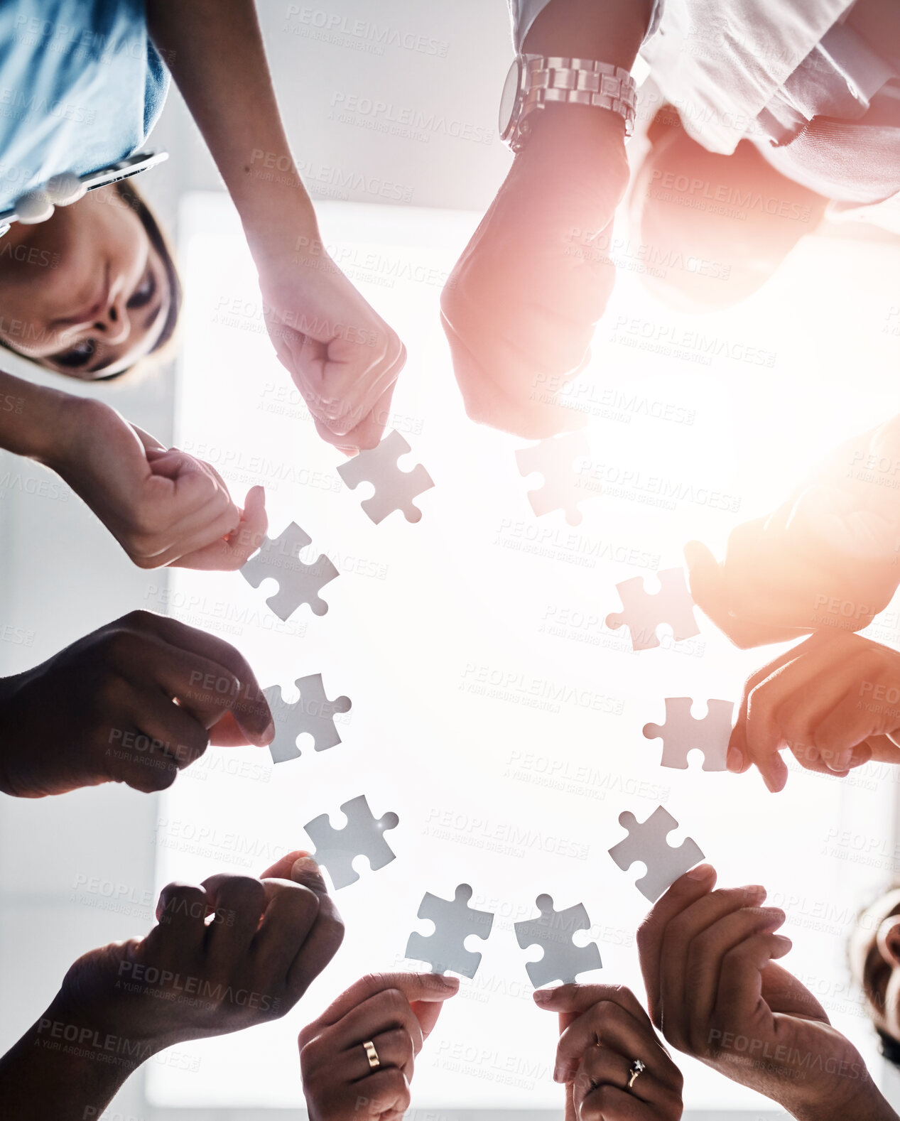 Buy stock photo Hands, puzzle piece and teamwork with people in huddle together for link, synergy or unity. Collaboration, partnership and support with group in circle from below for community, lens flare or trust