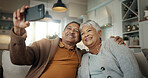 Senior couple, home and selfie while laughing on sofa and enjoying retirement together. Phone, smile and happy pensioners in family house, embracing each other and playful energy as elderly people