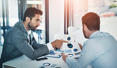 Buy stock photo Shot of two young businessmen going through paperwork together in a modern office