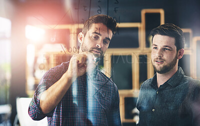 Buy stock photo Shot of two young businessmen using a digital tablet while brainstorming on a glass wall in an office