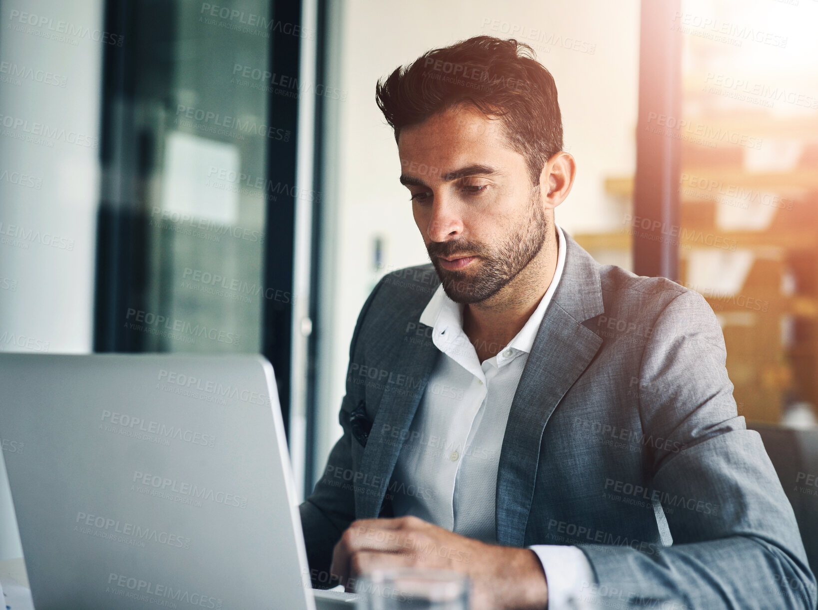 Buy stock photo Shot of a confident young businessman working on his laptop while being seated in the office during the day