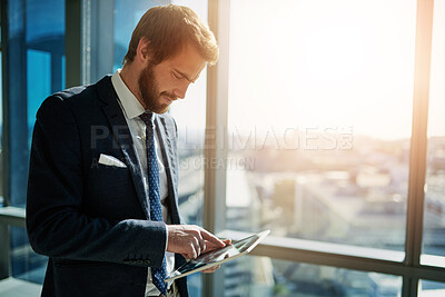 Buy stock photo Cropped shot of a handsome young businessman using a tablet in his office