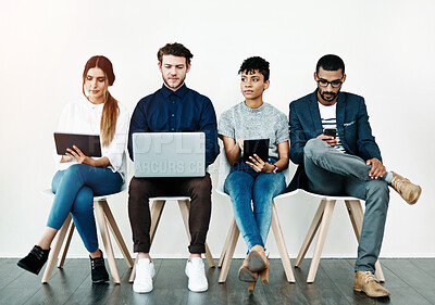 Buy stock photo Shot of a group of young people using wireless technology while sitting in a row