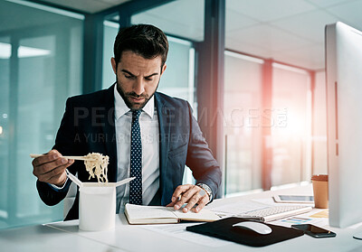 Buy stock photo Shot of a focused young businessman eating noodles while writing in a notebook inside of the office