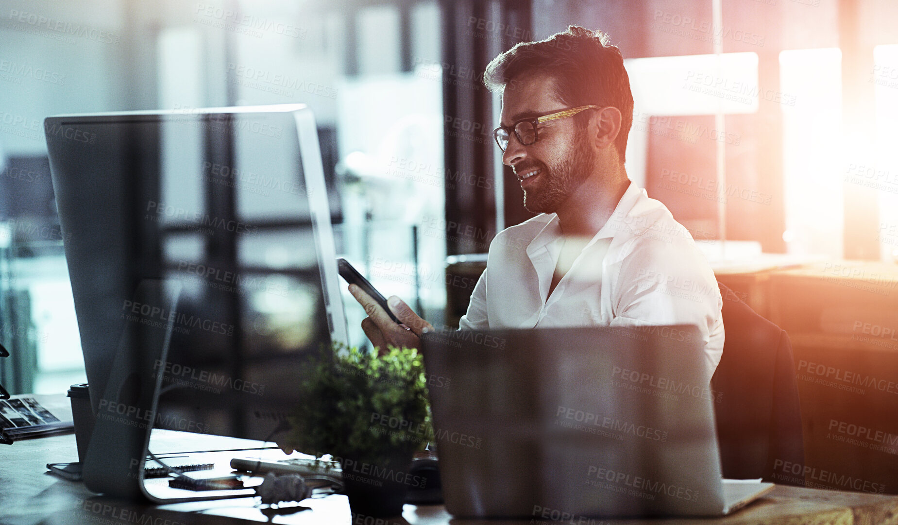 Buy stock photo Cropped shot of a handsome young businessman using his cellphone while working late in the office