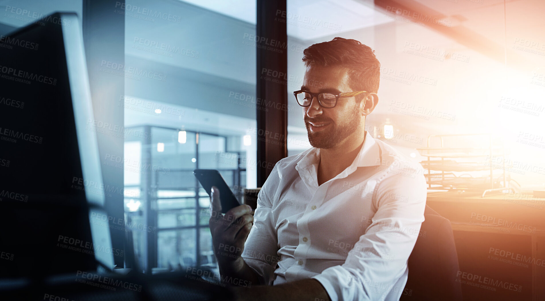 Buy stock photo Cropped shot of a handsome young businessman using his cellphone while working late in the office