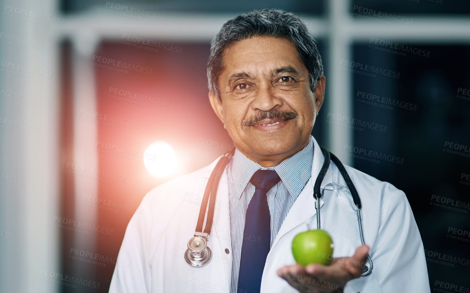 Buy stock photo Portrait of a mature doctor holding a green apple in a hospital