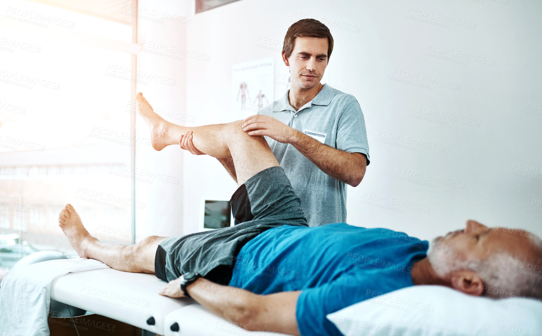 Buy stock photo Shot of a young male physiotherapist helping a client with leg exercises who's lying on a bed