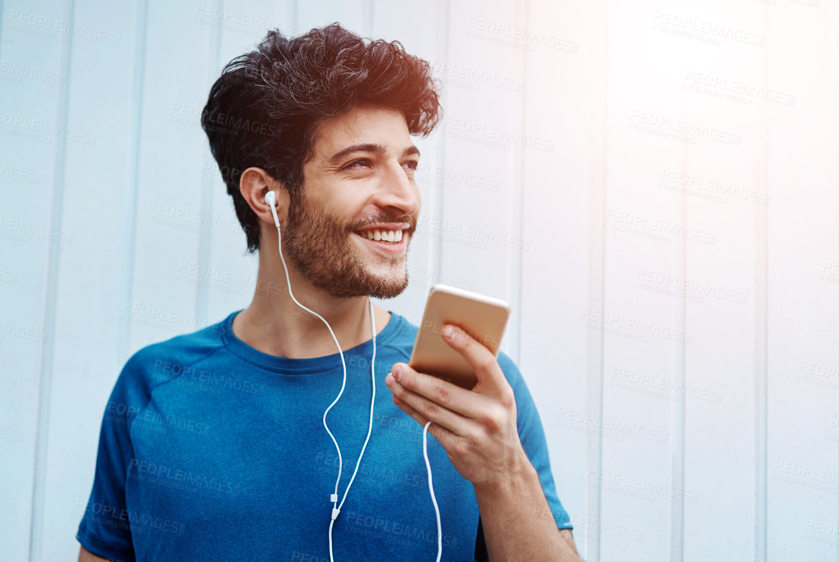 Buy stock photo Earphones, fitness and man with smartphone, wall and happiness with motivational podcast. Smile, person and athlete with cellphone, radio and online for audio, exercise and workout with lens flare 