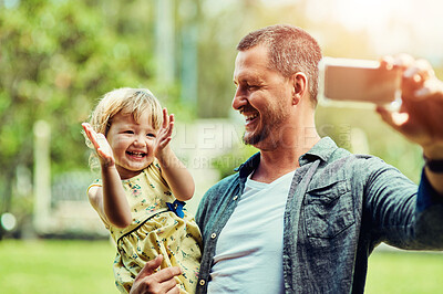 Buy stock photo Shot of a happy father and his adorable daughter taking selfies together outdoors