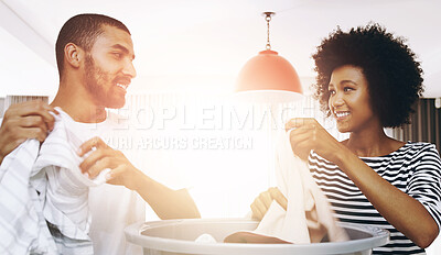 Buy stock photo Shot of a cheerful young couple working together and sorting out washing at home during the day