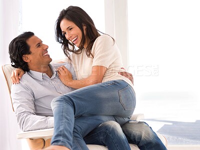 Buy stock photo Laughing, love and couple on chair in living room at home with comfortable romance and care. Happy, marriage and young man and woman sitting, talking and bonding together in lounge at modern house.