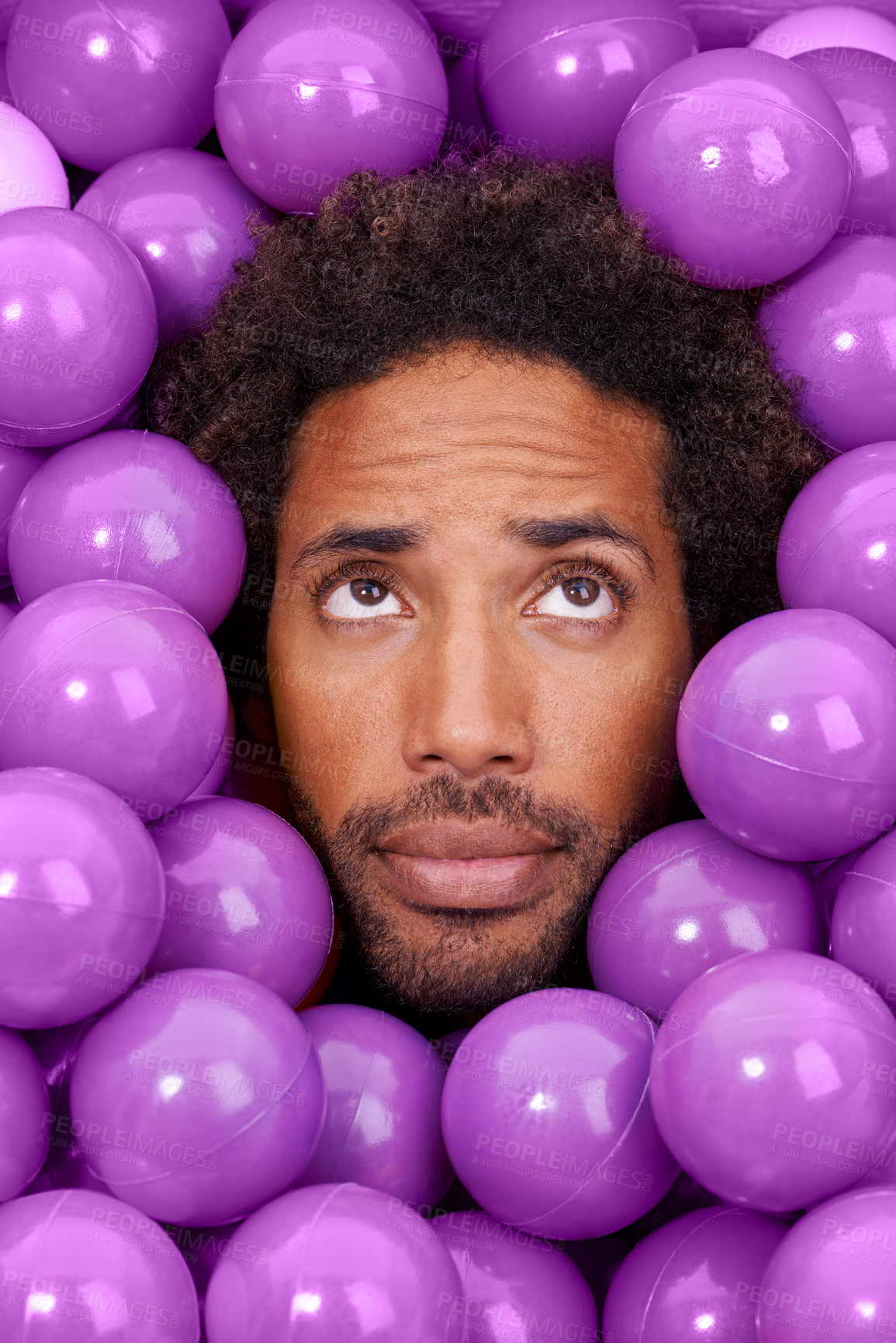 Buy stock photo Ball pit, thinking and face of black man with plastic toys for wondering, question and thoughtful on background. Confused, facial expression and person with purple balls, decoration and objects
