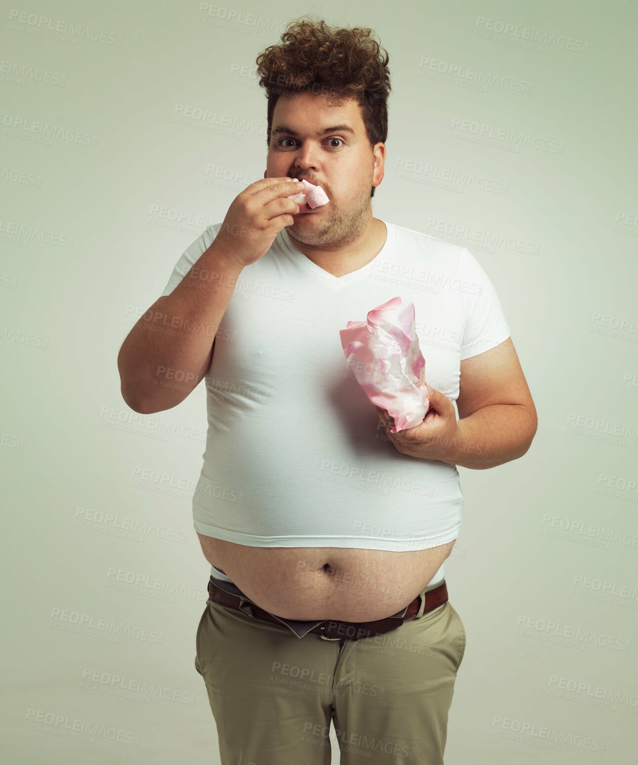 Buy stock photo Plus size, candy and portrait for man in studio with marshmallow for unhealthy eating, sugar and confection. Young person with sweets in mouth and round stomach for greed, comedy and humor indoor