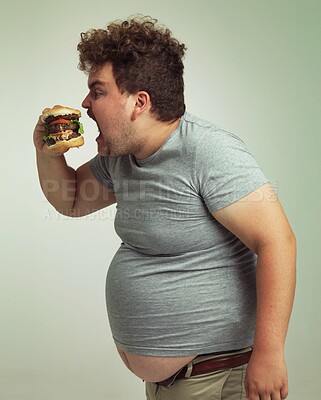 Buy stock photo Obesity, weight gain and fast food for man in studio with burger for unhealthy eating, plus size and greed. Overweight person with meal for mouth and fat stomach for hunger, comedy and bite indoor