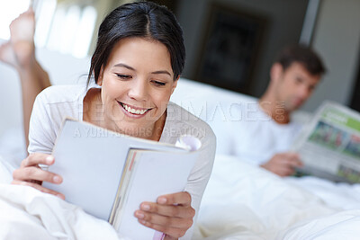 Buy stock photo Shot of a beautiful woman lying in bed reading a magazine 