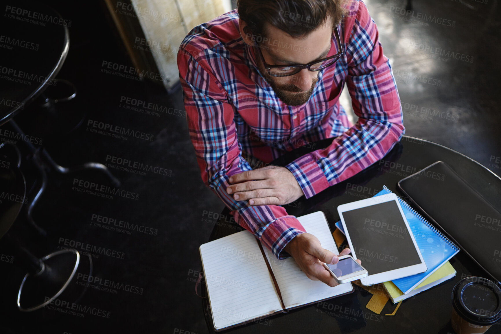 Buy stock photo Shot of a young man sitting at a table in a cafe with his cellphone, digital tablet and diary in front of him