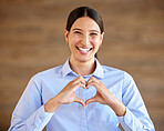 Young happy hispanic businesswoman smiling and standing and making a heart gesture with her hands alone at work. Cheerful and positive mixed race female making a heart with her hands in an office