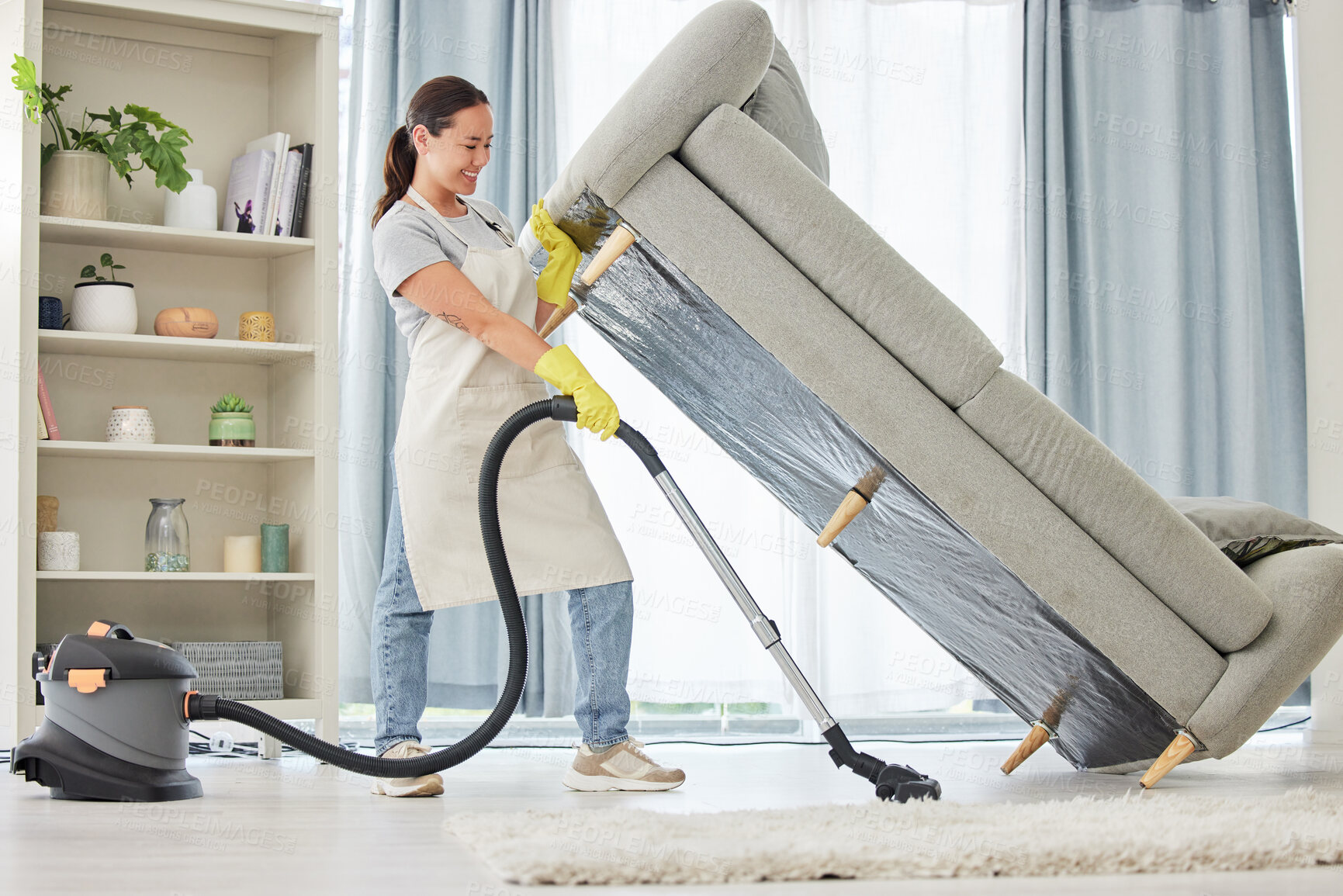 Buy stock photo Woman, vacuum and lifting sofa in living room for spring cleaning, hygiene and housekeeping in home. Maid, domestic worker or female person with machine for service, remove dirt or household chores